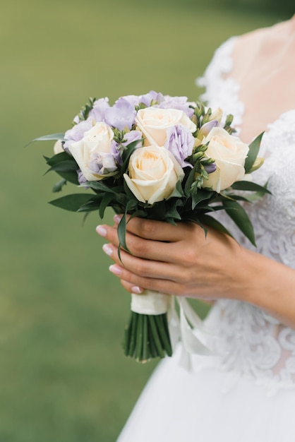 O buquê de noivas de rosas de leite e eustoms lilás nas mãos da noiva