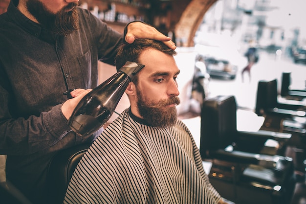 cabeleireiro secando o cabelo de seu cliente com um secador de