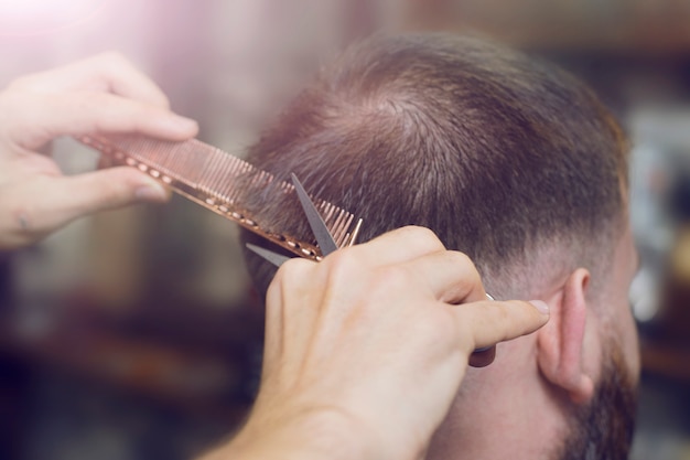 O cabeleireiro faz um corte de cabelo para um homem, mãos close-up, foco seletivo.