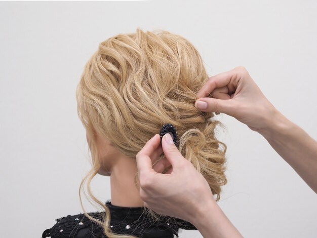 O cabeleireiro faz um penteado de casamento para a noiva com um acessório de cabelo