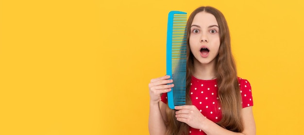 O cabelo comprido da criança espantado segura a escova de cabelo no cabeleireiro de fundo amarelo Cuidados com o cabelo da menina na horizontal