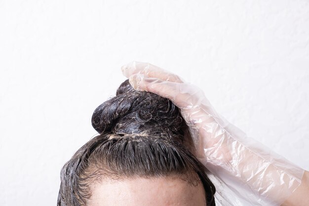 O cabelo das mulheres é coletado em um coque com tinta aplicada a ele e mão enluvada Conceito de tingimento de cabelo