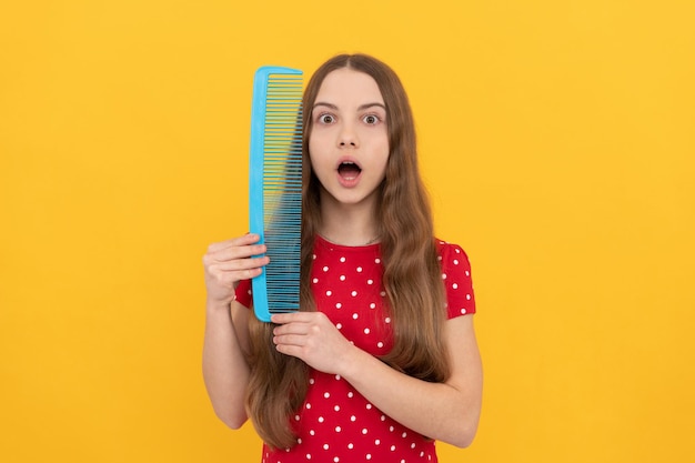 O cabelo longo da criança espantado segura a escova de cabelo no cabeleireiro de fundo amarelo