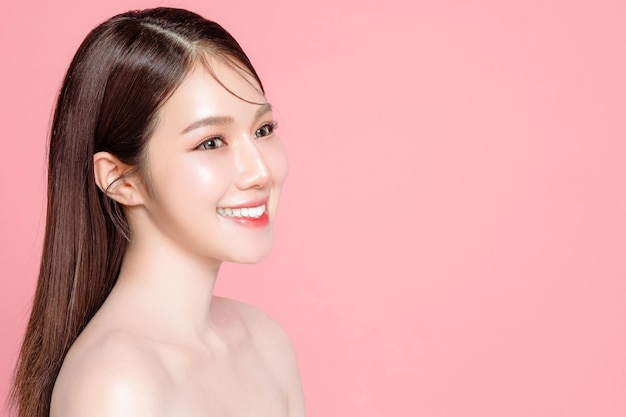 O cabelo longo da jovem mulher asiática com maquiagem natural no rosto tem lábios carnudos e pele limpa e fresca em fundo rosa isolado Retrato de modelo feminino bonito em estúdio Tratamento facial Cosmetologia