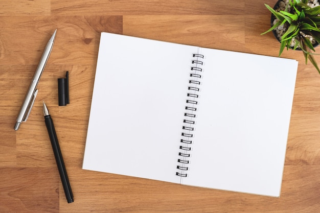 Foto o caderno vazio está sobre a tabela de madeira da mesa de escritório com penas.