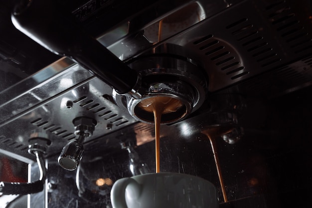 O café é derramado da máquina de café na xícara branca de preparação de café profissional