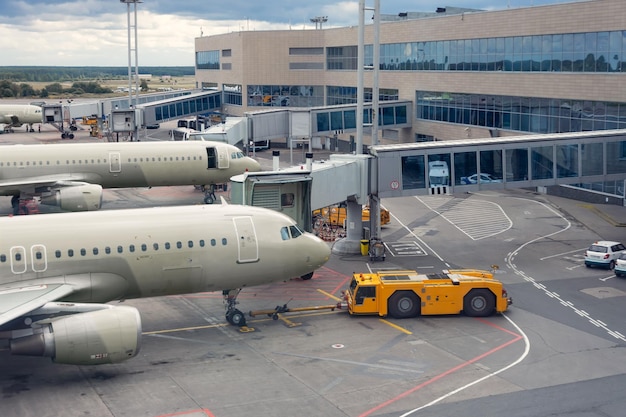 Foto o caminhão pushback está rebocando a aeronave para um estacionamento em uma fileira de aviões ao longo do edifício do terminal