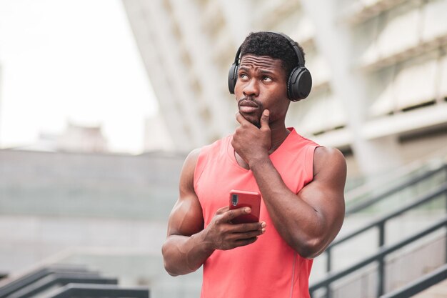 O cara afro-americano pensativo em fones de ouvido ouve música e pensa