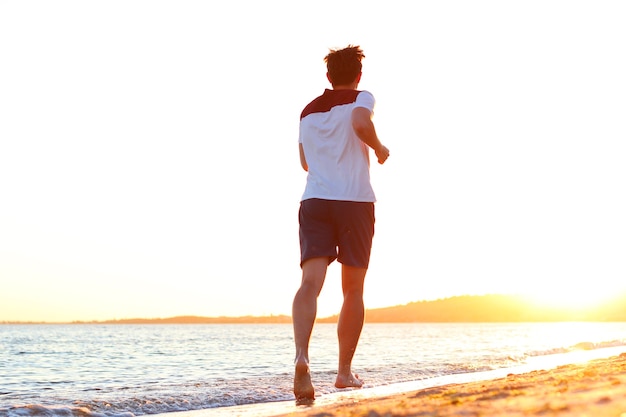 O cara corre à beira-mar contra o pôr do sol