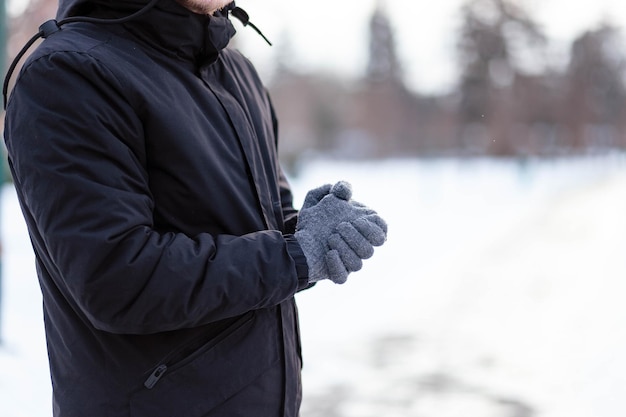 O cara de luvas aquece as mãos o cara aquece as mãos mãos de luvas de inverno cinza a palma com a luva na neve