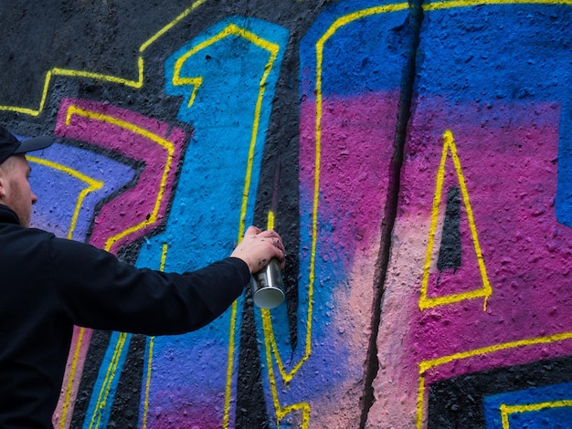 O cara desenha um graffiti colorido brilhante em uma parede preta