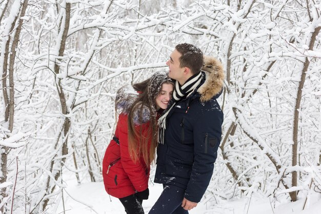 O cara e a garota descansam na floresta de inverno Marido e mulher na neve Casal jovem caminhando no parque de inverno