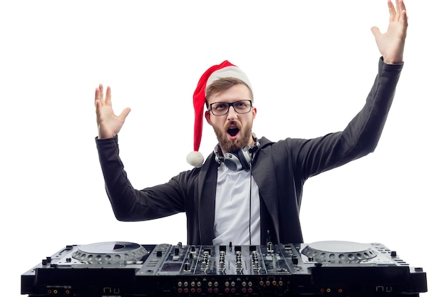 O cara engraçado gritando DJ usando óculos de chapéu de Papai Noel toca música em uma plataforma giratória levanta as mãos e levanta a foto do estúdio