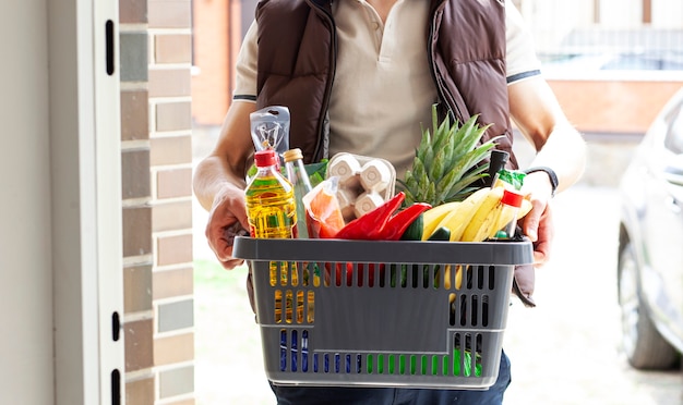 O cara entrega a cesta cheia de mantimentos na porta da casa. compras online.