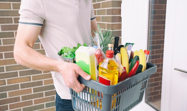 O cara entrega a cesta cheia de mantimentos na porta da casa. Compras online.