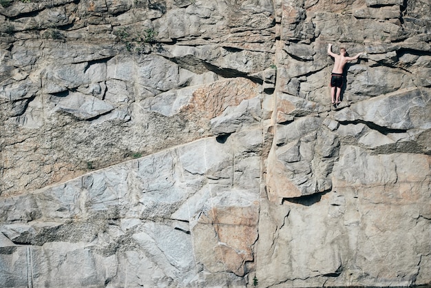 Foto o cara está escalando pedras e olha em cima, extremo. superfície com crista, em fendas