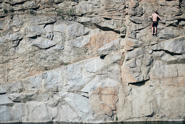 Foto o cara está escalando pedras e olha em cima, extremo. superfície com crista, em fendas