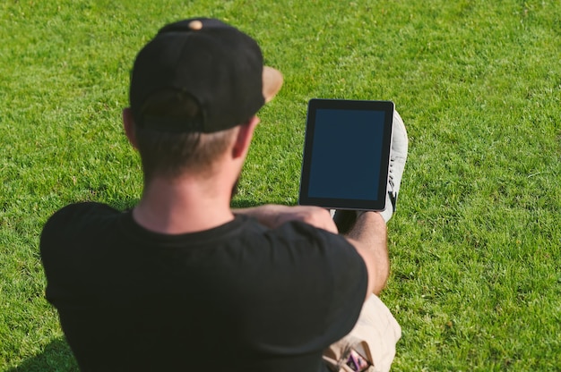O cara está fazendo um treinamento online, em um gramado verde com um tablet.