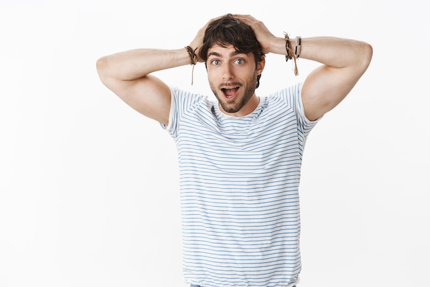 O cara não pode acreditar que um milagre pode acontecer. Retrato de namorado atraente sem palavras impressionado e surpreso com homens, olhos azuis e barba de mãos dadas na cabeça de espanto, deixando cair o queixo.