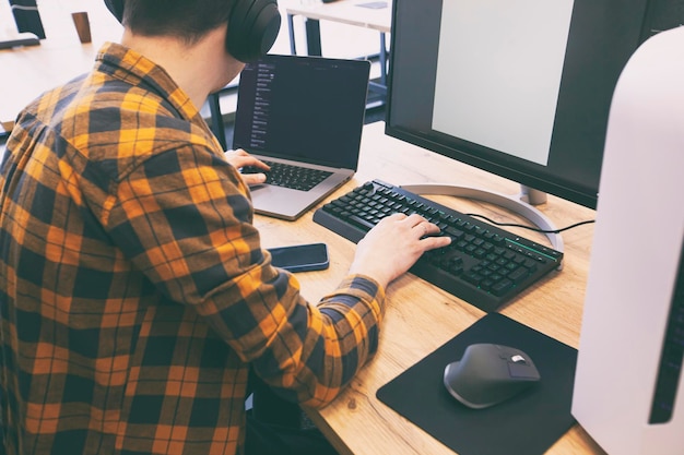 Foto o cara no escritório trabalhando com o laptop e pc ao mesmo tempo