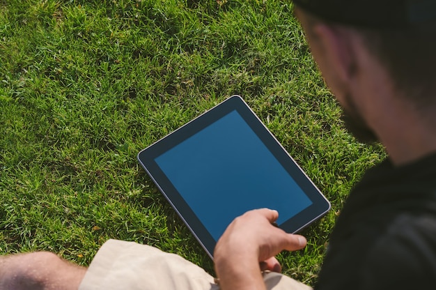 O cara olha para o tablet caído no gramado.