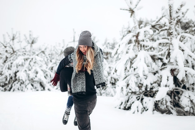 O cara segura a garota nos braços na floresta de neve de inverno