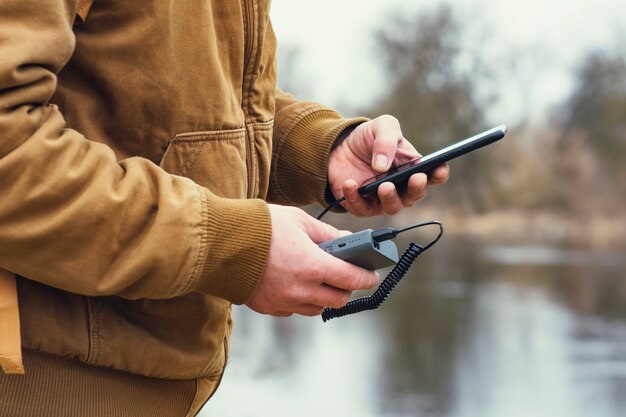 O cara segura um carregador portátil com um smartphone na mão. Um homem no fundo de um lago carrega o telefone com o Power Bank. Conceito sobre o tema do turismo.