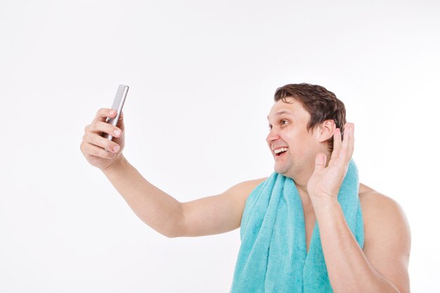 O cara tira uma selfie após os procedimentos matinais. um homem olha para a câmera do telefone. rosto bem barbeado. toalha azul em volta do pescoço. homem e tecnologias modernas. a conversa via link de vídeo