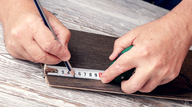 O carpinteiro usa uma fita métrica para marcar a placa de madeira