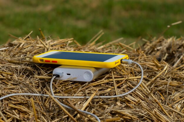 O carregador portátil carrega um smartphone ao ar livre em um campo contra um fundo de feno.