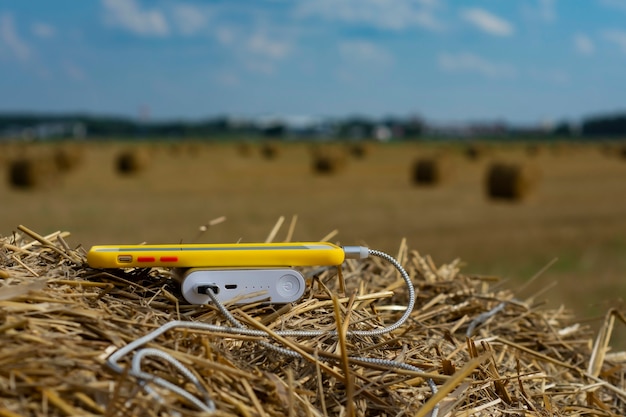 O carregador portátil carrega um smartphone ao ar livre em um campo contra um fundo de feno.