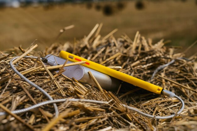 O carregador portátil carrega um smartphone ao ar livre em um campo contra um fundo de feno.