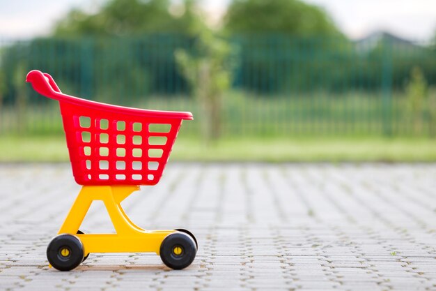 O carrinho de compras colorido plástico brilhante brinca fora no dia de verão ensolarado.