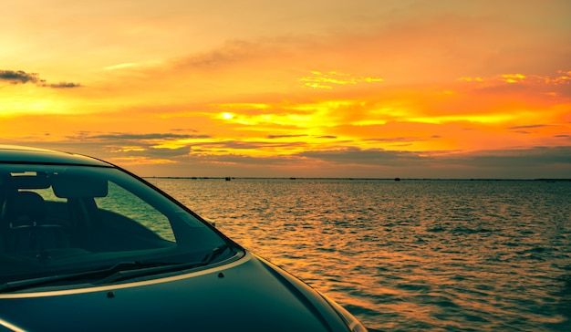 O carro azul de suv com esporte e projeto moderno estacionou na estrada concreta pelo mar no por do sol.