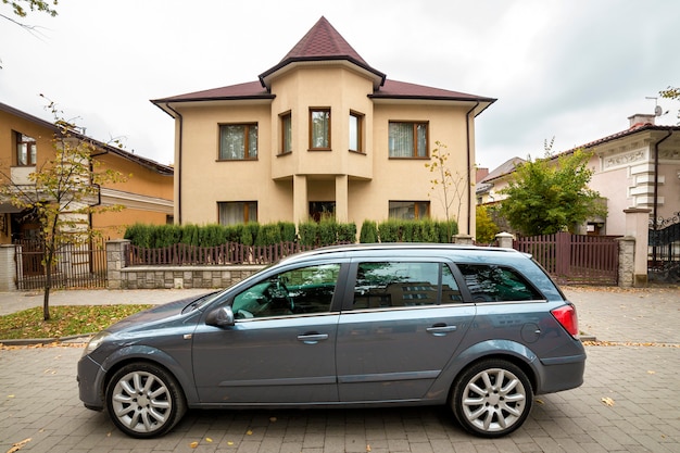 O carro cinza novo e caro estacionou no estacionamento pavimentado em frente à grande casa de dois andares.