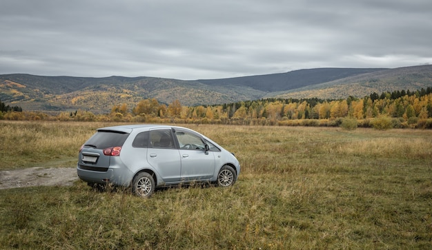 O carro está estacionado em um gramado em frente às colinas e à pitoresca floresta de outono verde-amarelo. Conceito de viagem, bela natureza e clima de outono