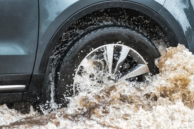 O carro está passando por uma poça na chuva forte salpicos de água debaixo das rodas de um carro inundação e água alta na cidade