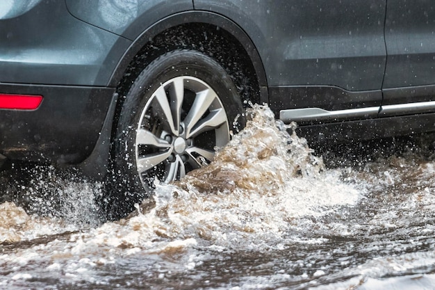 O carro está passando por uma poça na chuva forte Salpicos de água debaixo das rodas de um carro Inundação e água alta na cidade