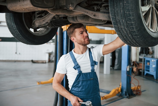 O carro moderno está sendo reparado. Empregada com uniforme azul trabalha no salão automóvel.