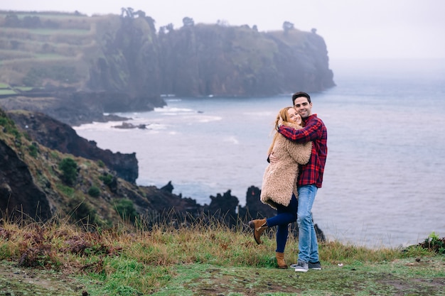 O casal apaixonado abraça e sorri na costa do oceano.