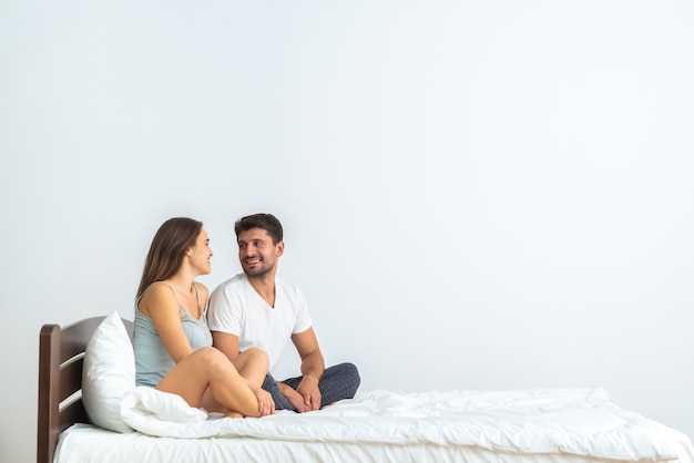 O casal atraente sentado na cama, no fundo branco