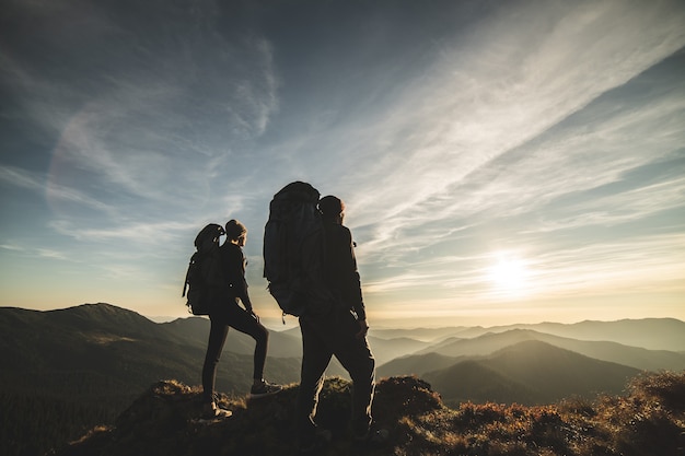 O casal em pé na montanha com um cenário pitoresco ao pôr do sol