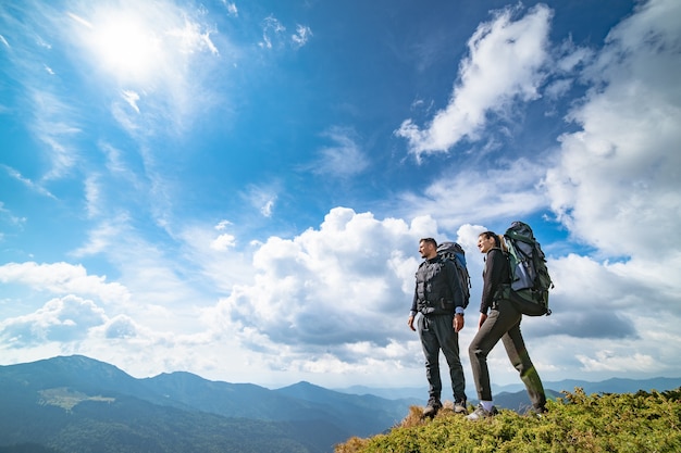 O casal em pé na montanha com uma paisagem pitoresca de nuvens