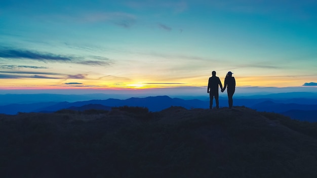 O casal em pé na montanha, no fundo do sol