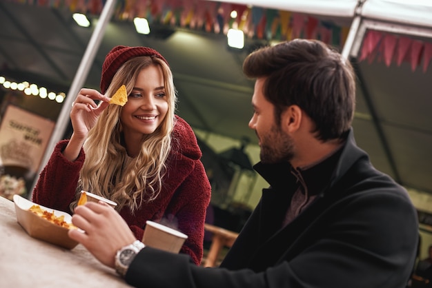 O casal está bebendo ao ar livre. Jovem casal está bebendo vinho quente com lanches no mercado de comida de rua. Estação fria. Foto de close-up de casal