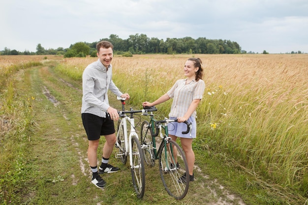 O casal feliz andando de bicicleta perto do campo