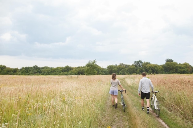 O casal feliz andando de bicicleta perto do campo