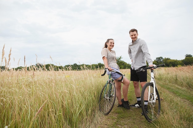 O casal feliz andando de bicicleta perto do campo