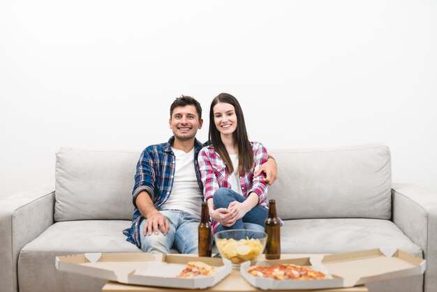 O casal feliz assistindo tv com uma pizza e uma cerveja no fundo branco