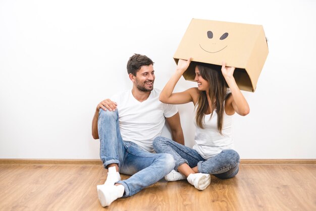 Foto o casal feliz com uma caixa de papelão senta no chão